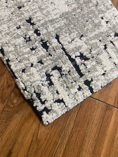 Cream and black patterned rug corner with a rolled edge on a wood floor