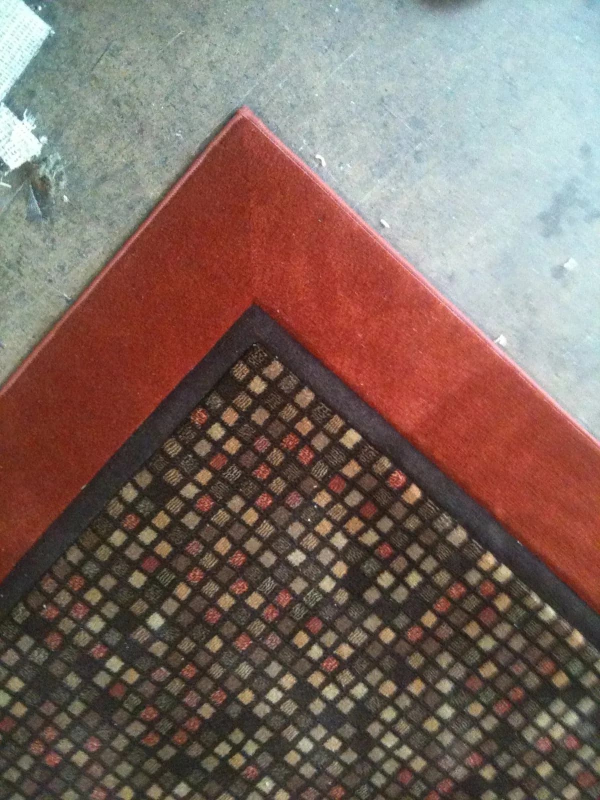 Multicolored square-patterned rug with a dark inner band and a wide red border, seamed and beveled at the corner