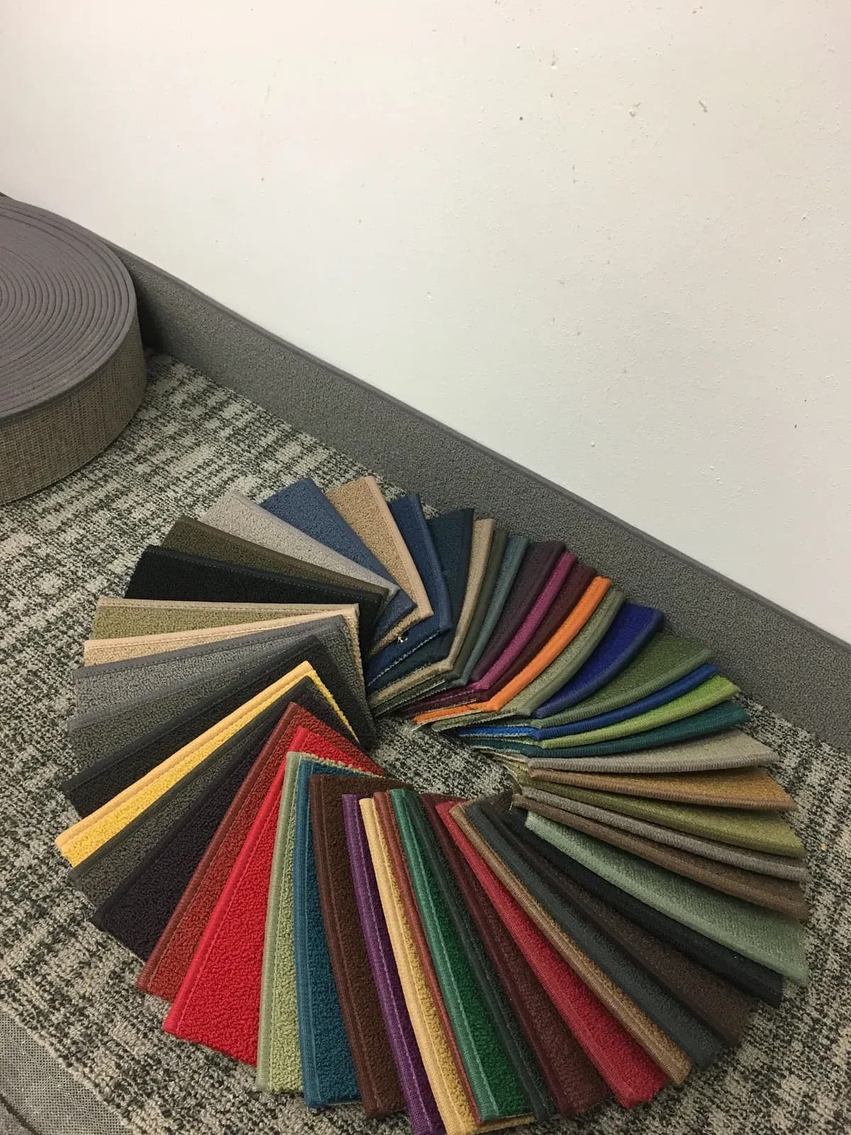 Carpet cove base samples in assorted colors beside a roll of base and gray base installed along a wall